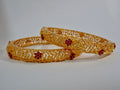 Pair of gold bangles with red stones on a white background