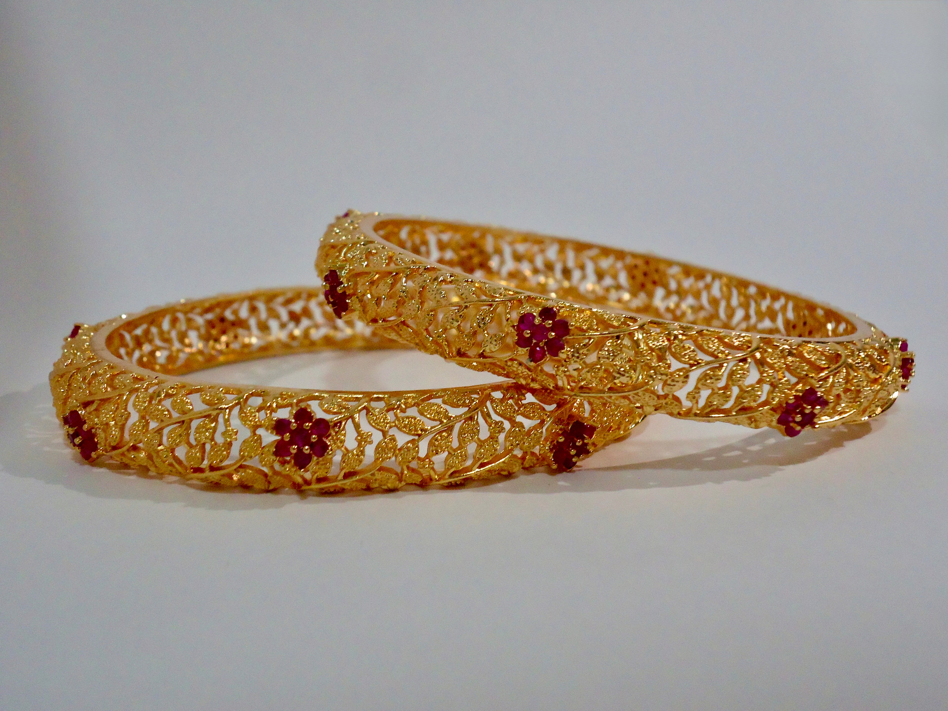 Pair of gold bangles with red stones on a white background