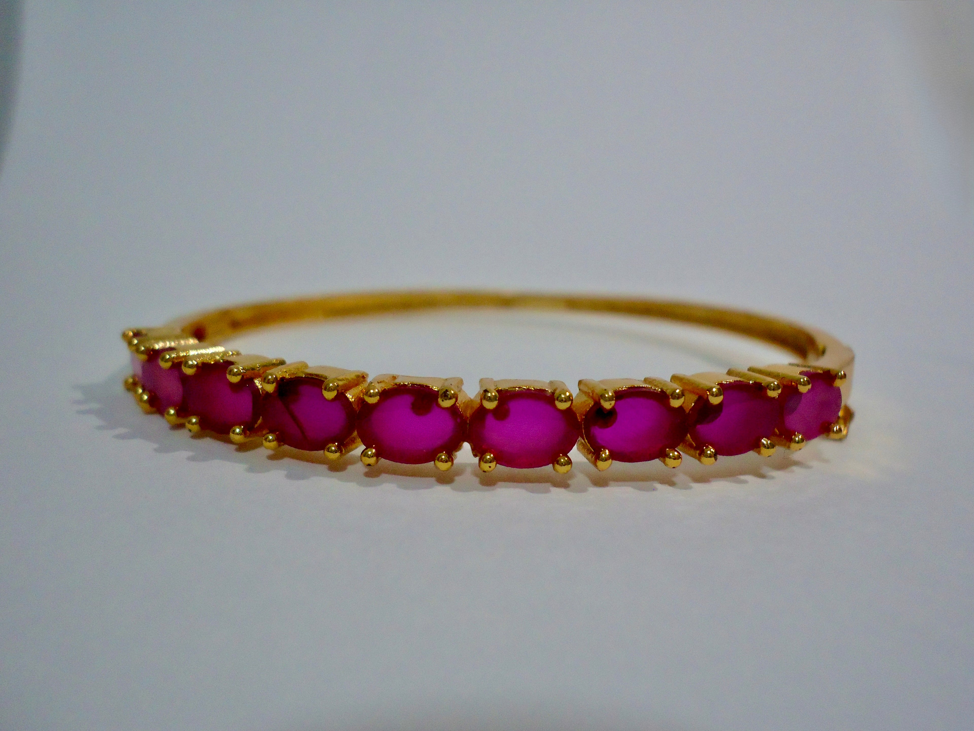 Gold bracelet with red gemstones on a white background