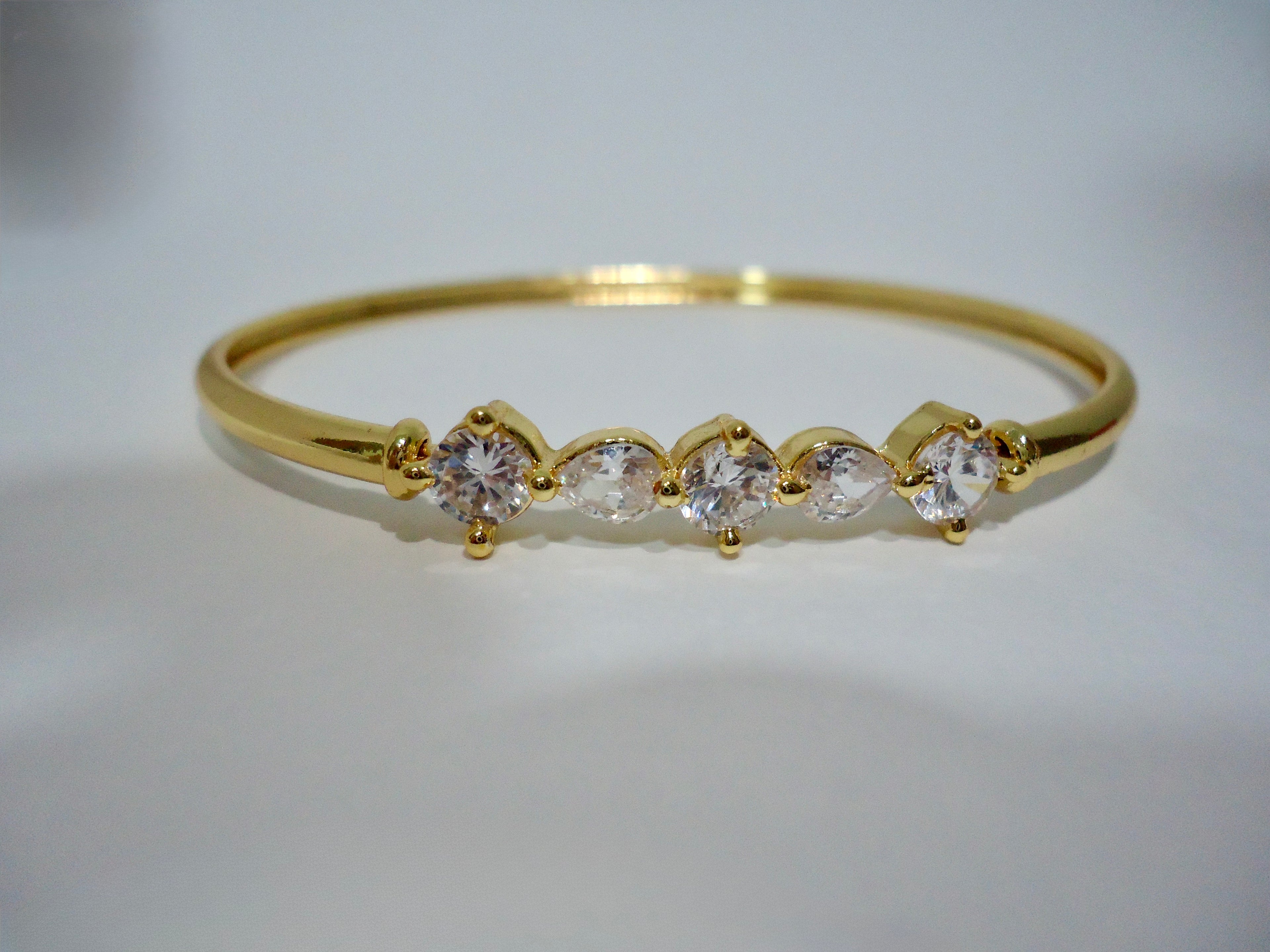 Gold bracelet with clear gemstones on a white background