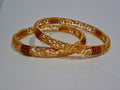 Two gold bangles with red stones on a white background