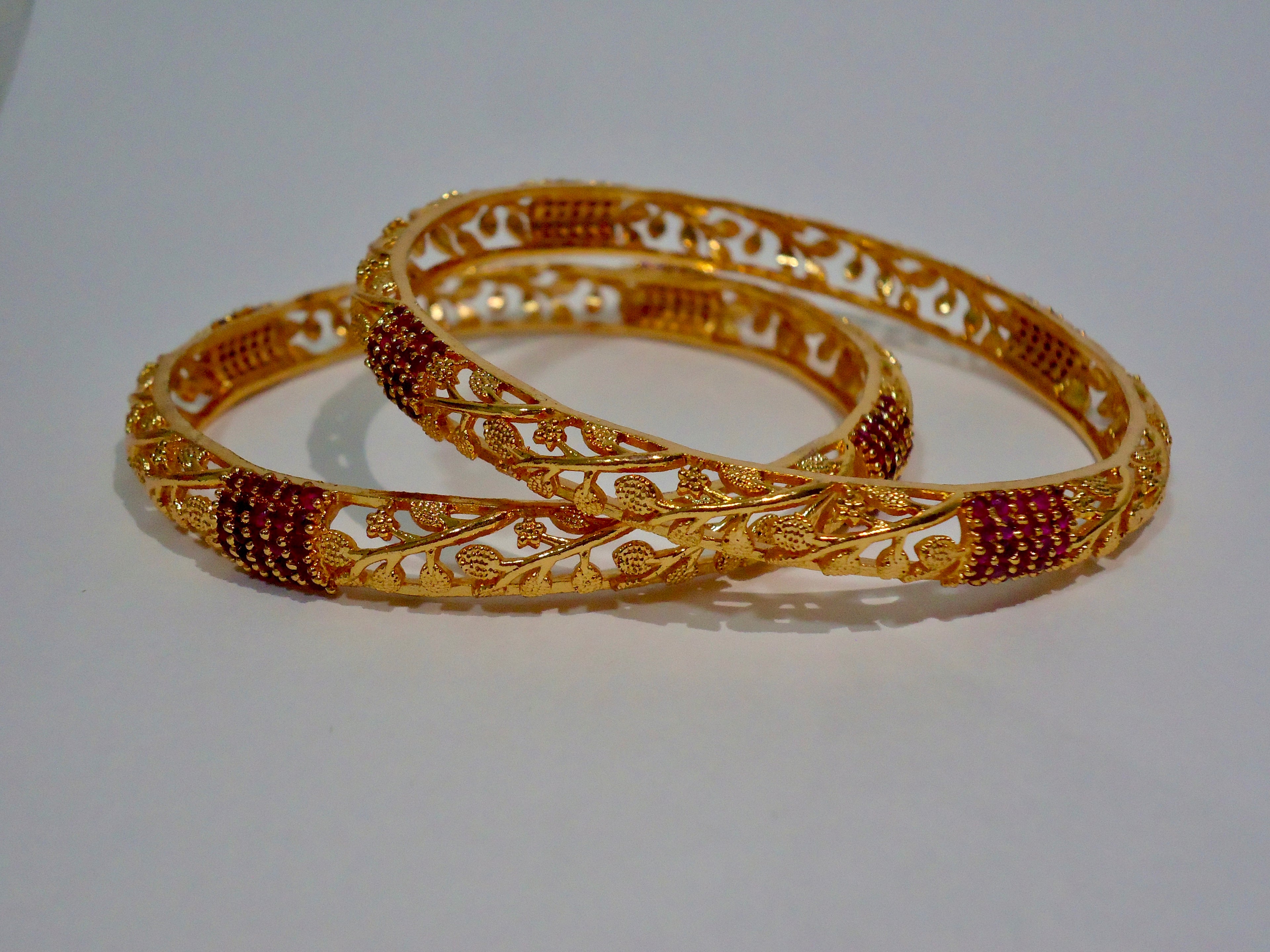 Two gold bangles with red stones on a white background
