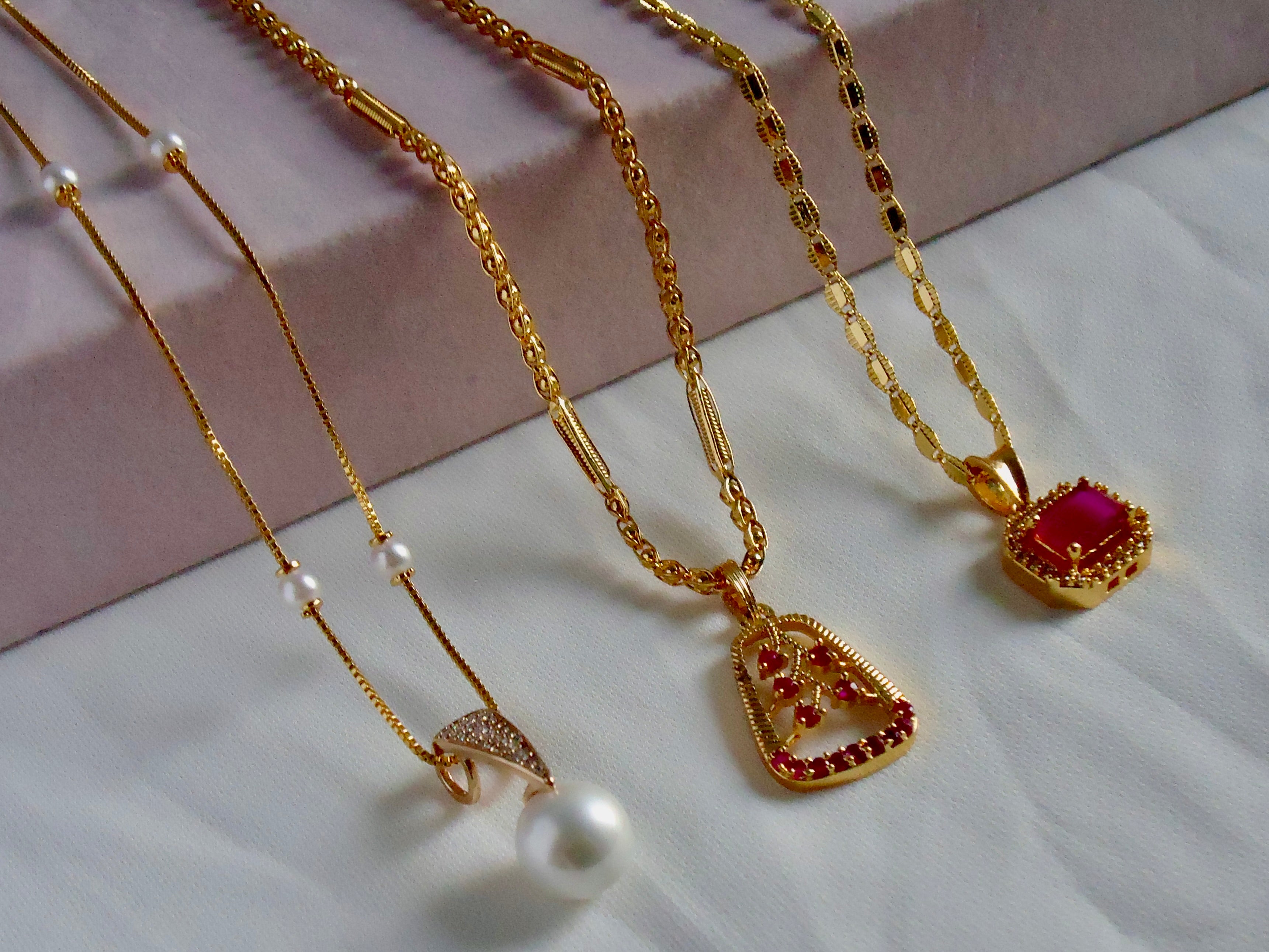 Three gold necklaces with various pendants on a light cream and white background