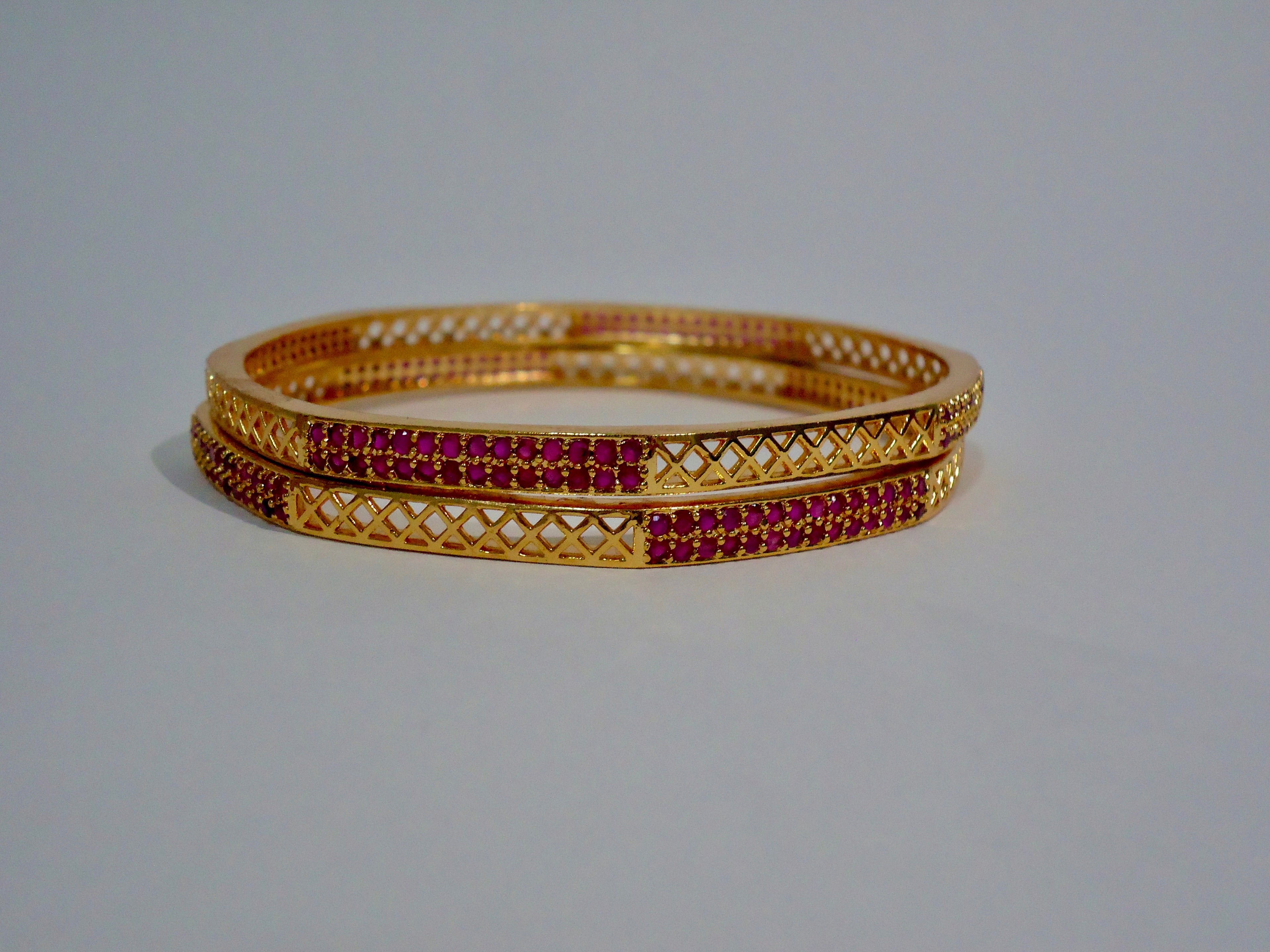 Gold bangles with red stones on a white background