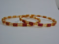 Gold bangles with red gemstones on a white background