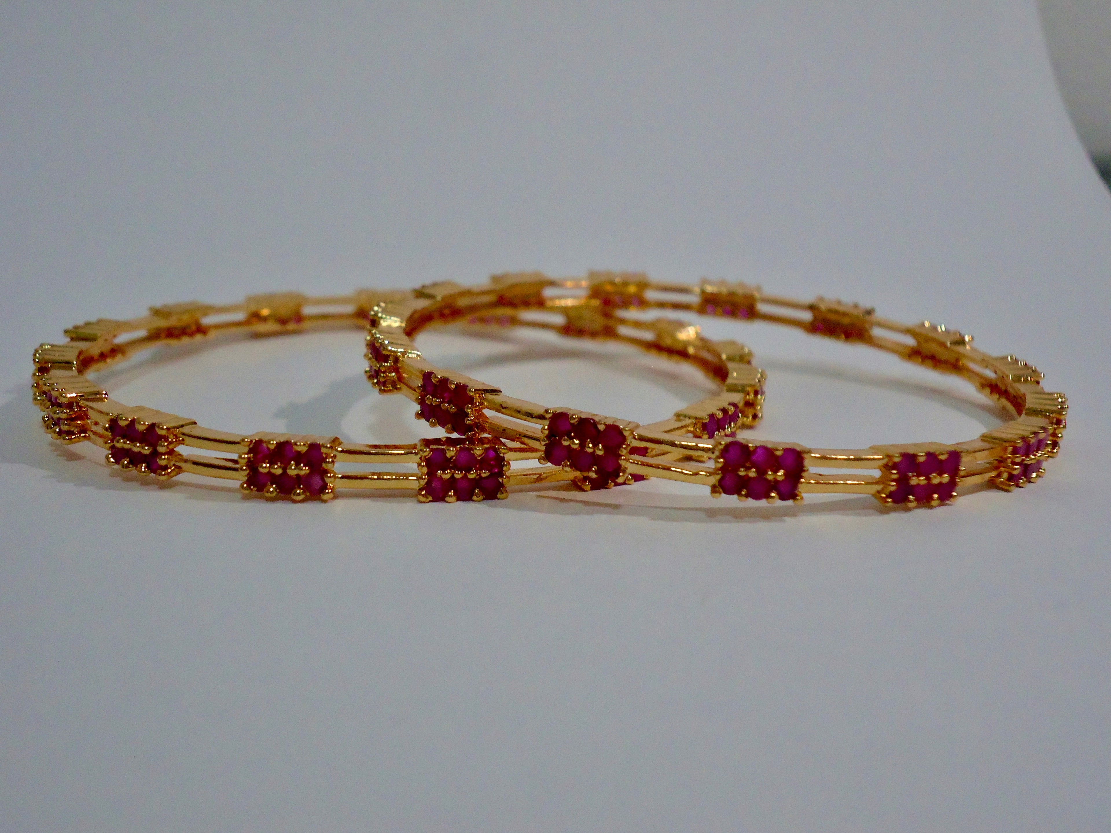 Gold bangles with red gemstones on a white background