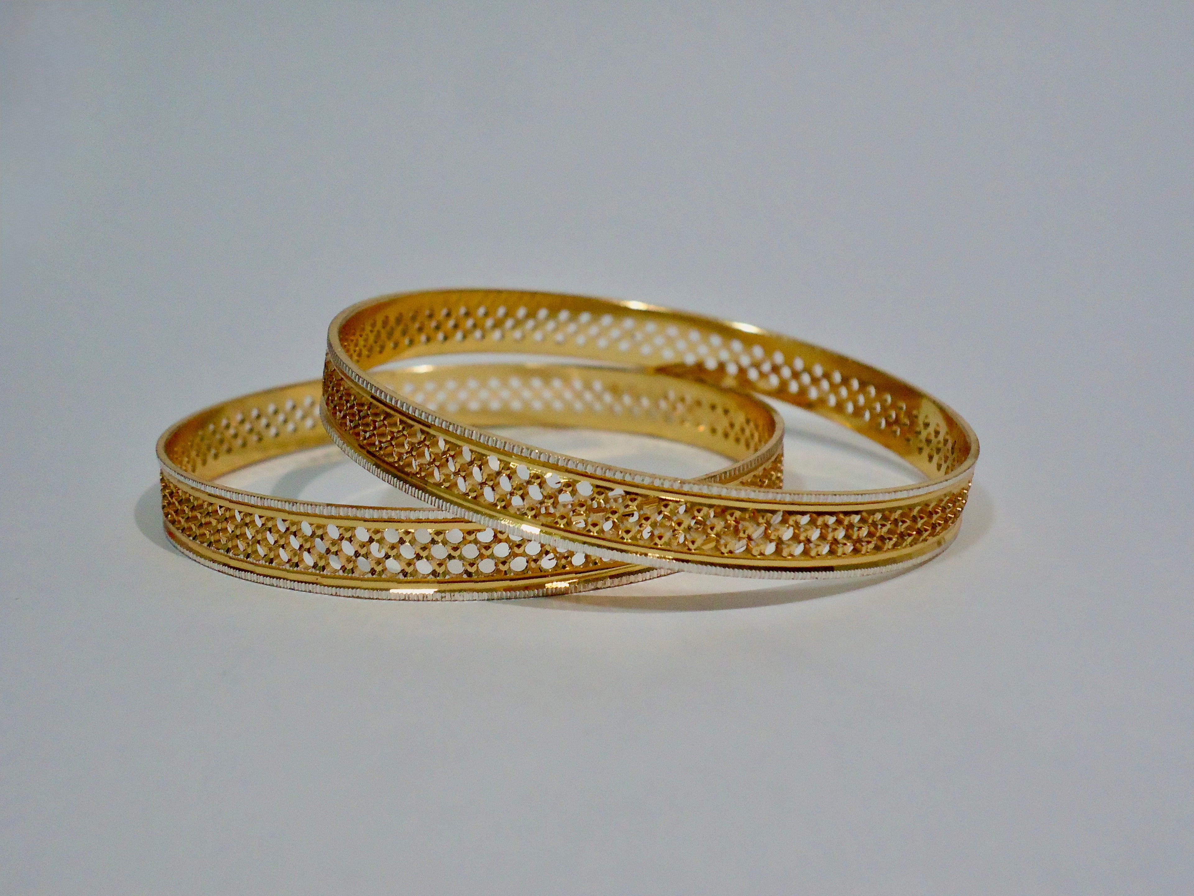 Two gold bangles with intricate designs on a white background